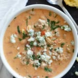 White bowl filled with Buffalo Chicken Chili made with ground chicken, and topped with blue cheese and minced cilantro.