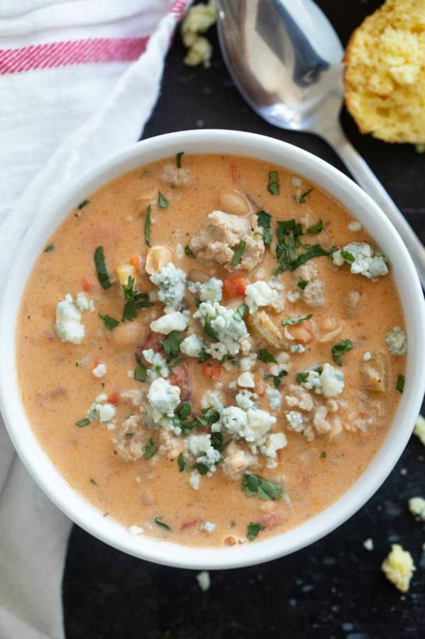 White bowl filled with Buffalo Chicken Chili made with ground chicken, and topped with blue cheese and minced cilantro.