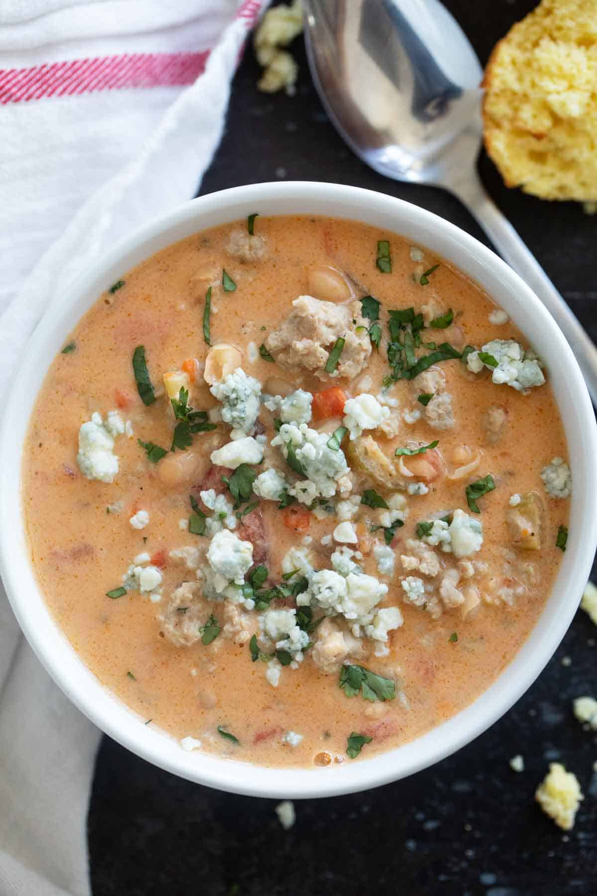 White bowl filled with Buffalo Chicken Chili made with ground chicken, and topped with blue cheese and minced cilantro.