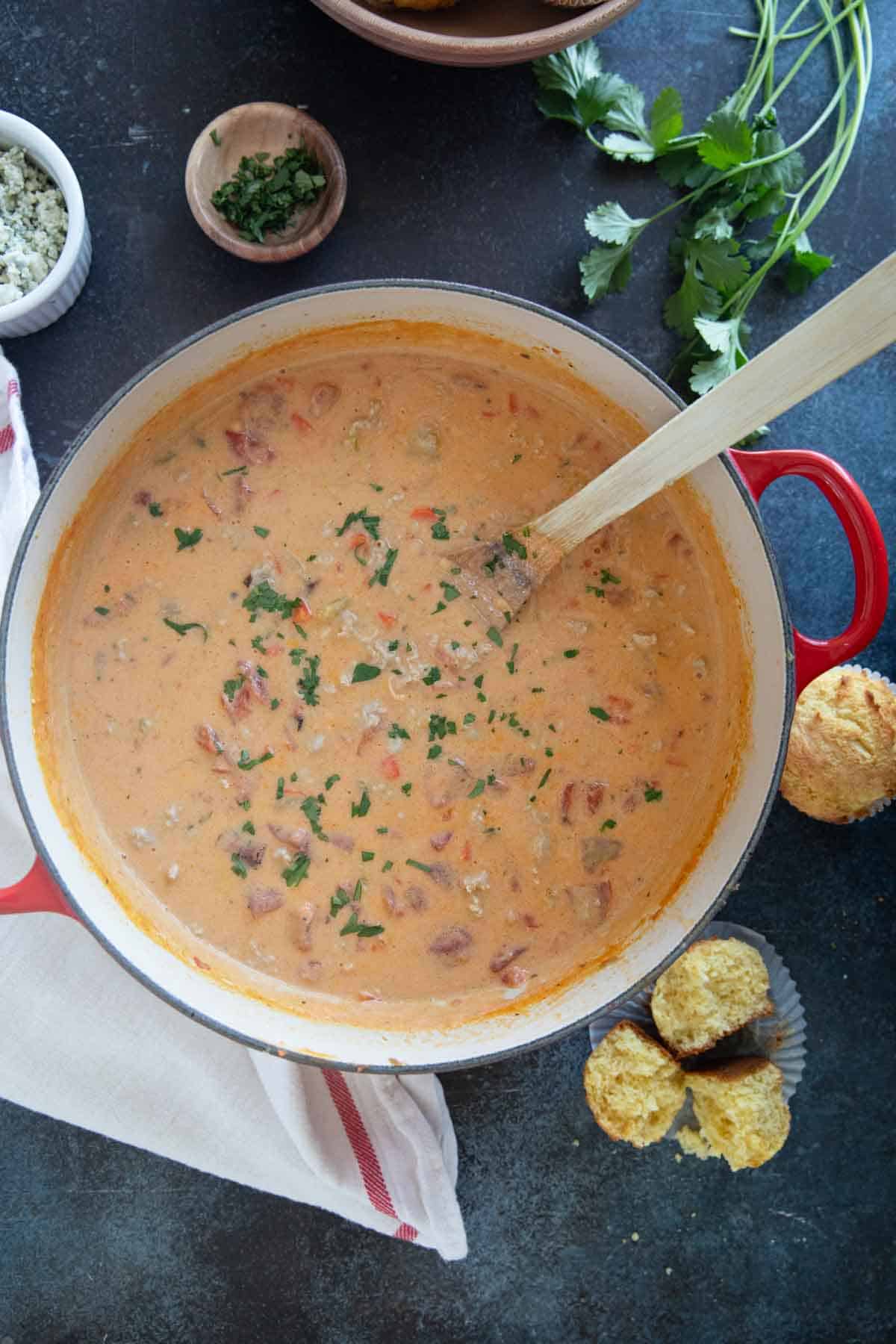 Pot full of Buffalo Chicken Chili, surrounded by corn muffins, cilantro, and blue cheese.