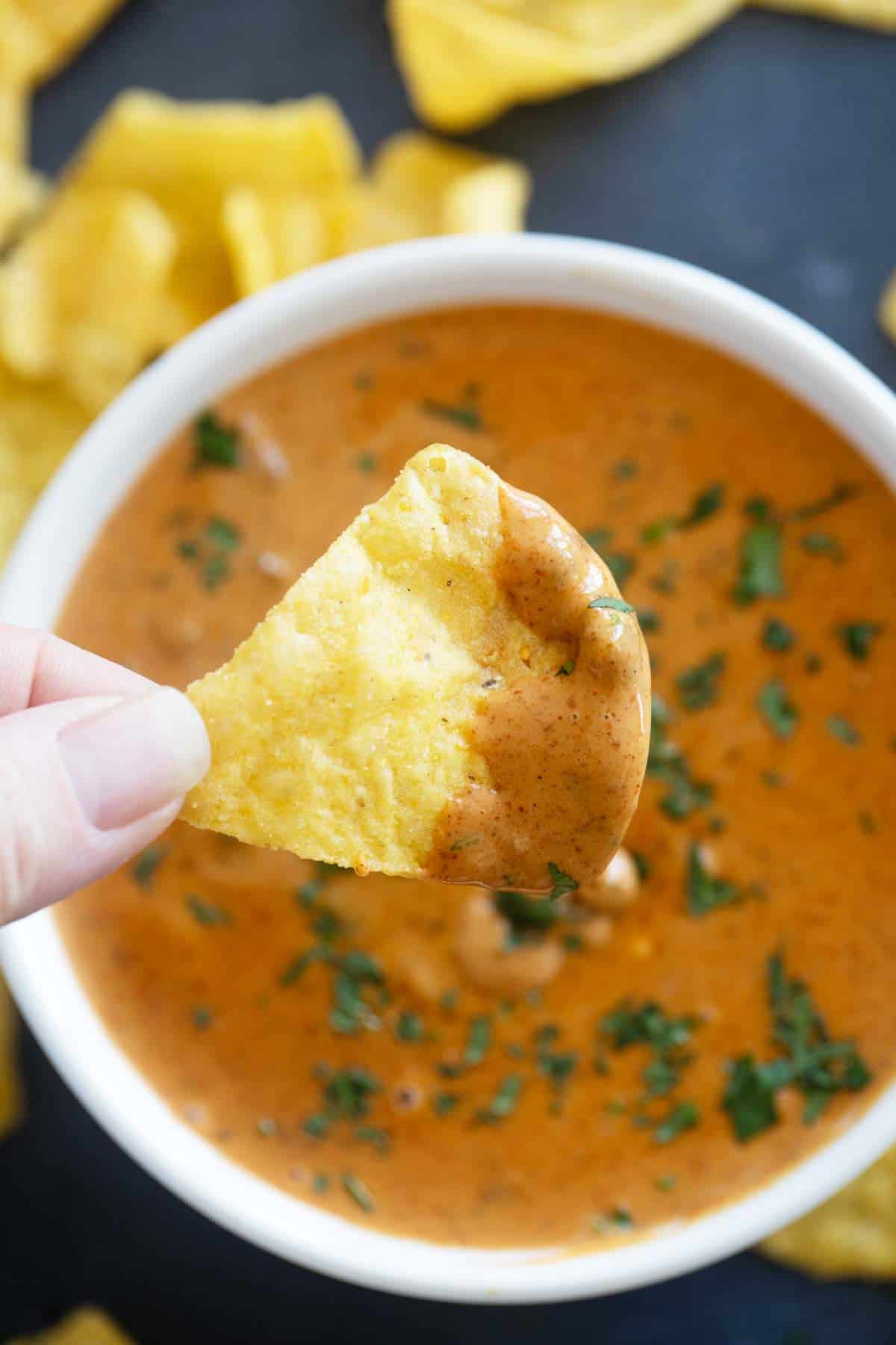 Chip with Chili's Queso Dip on it, over a bowl of queso.