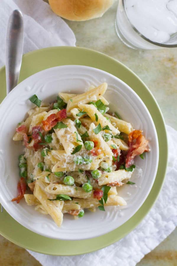 White bowl with one pan pasta with bacon and peas, topped with parmesan cheese.