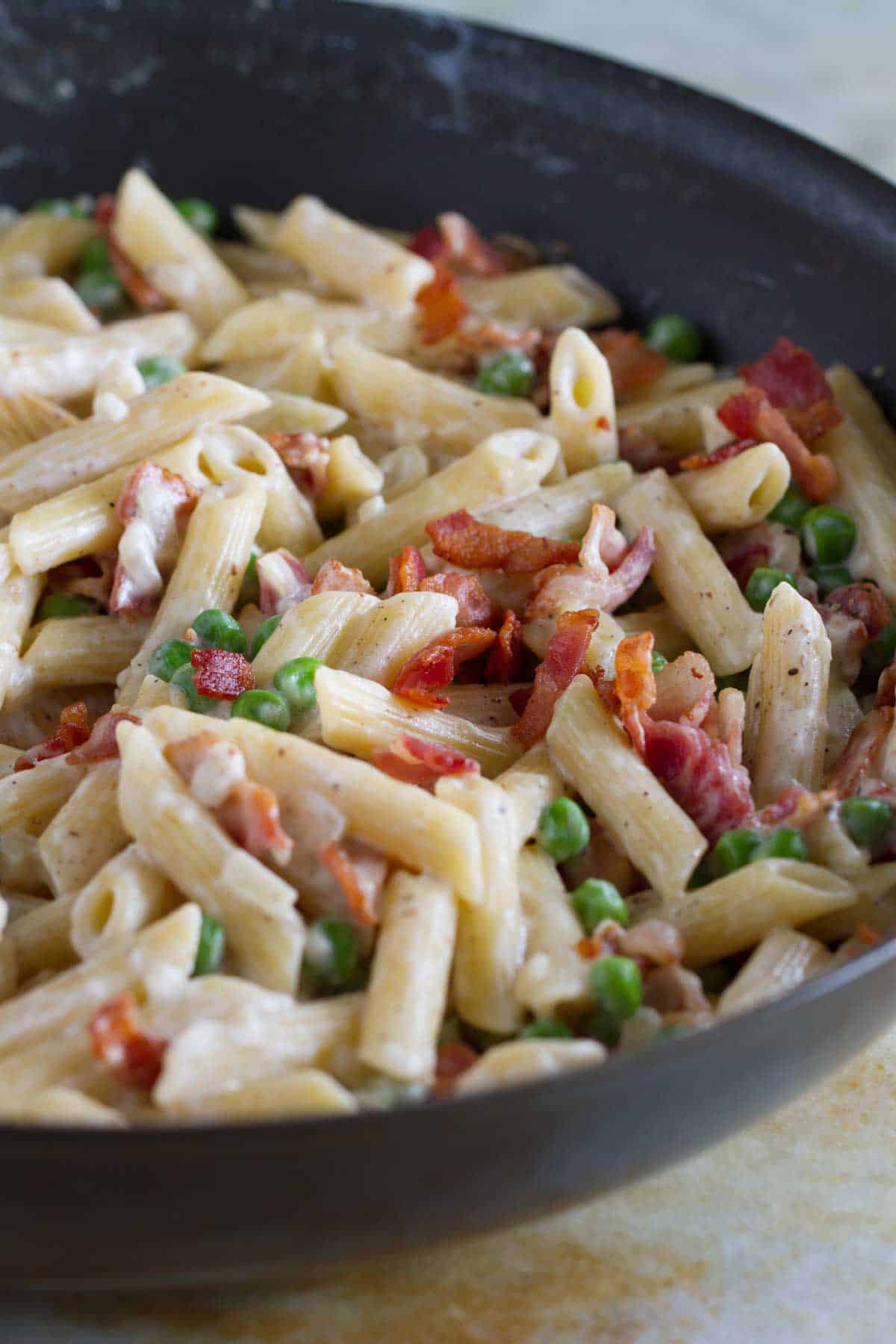 Pasta with bacon and peas in a skillet.