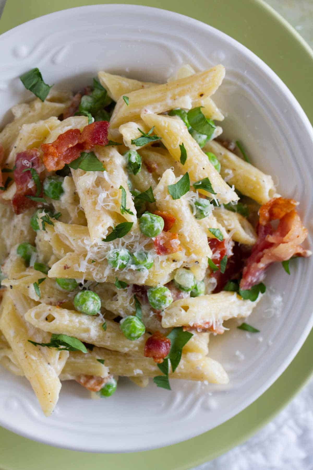 Shallow bowl with pasta with cream sauce, bacon, and peas.