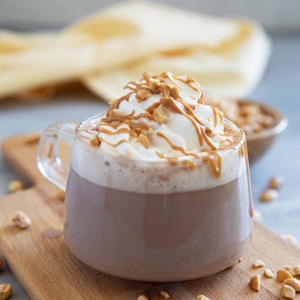 Glass mug filled with peanut butter hot chocolate, topped with whipped cream, peanut butter, and chopped peanuts.