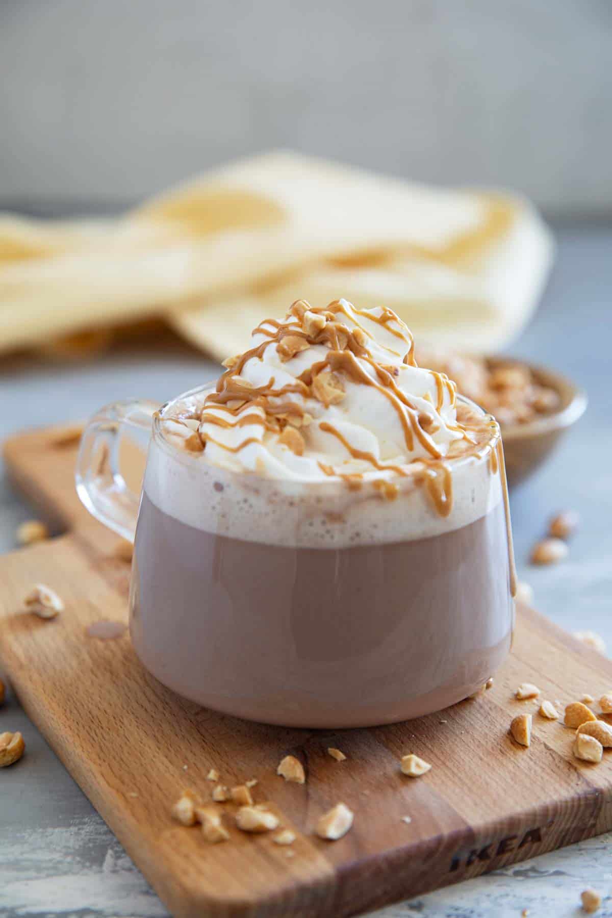 Glass mug filled with peanut butter hot chocolate, topped with whipped cream, peanut butter, and chopped peanuts.