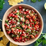 Wooden bowl filled with pico de Gallo, with chips and vegetables around the bowl.