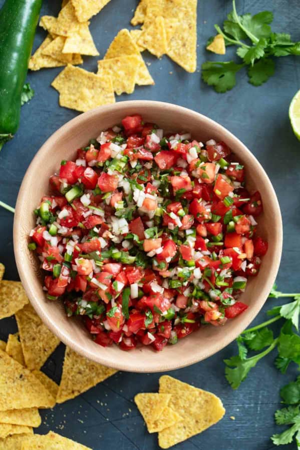 Wooden bowl filled with pico de Gallo, with chips and vegetables around the bowl.