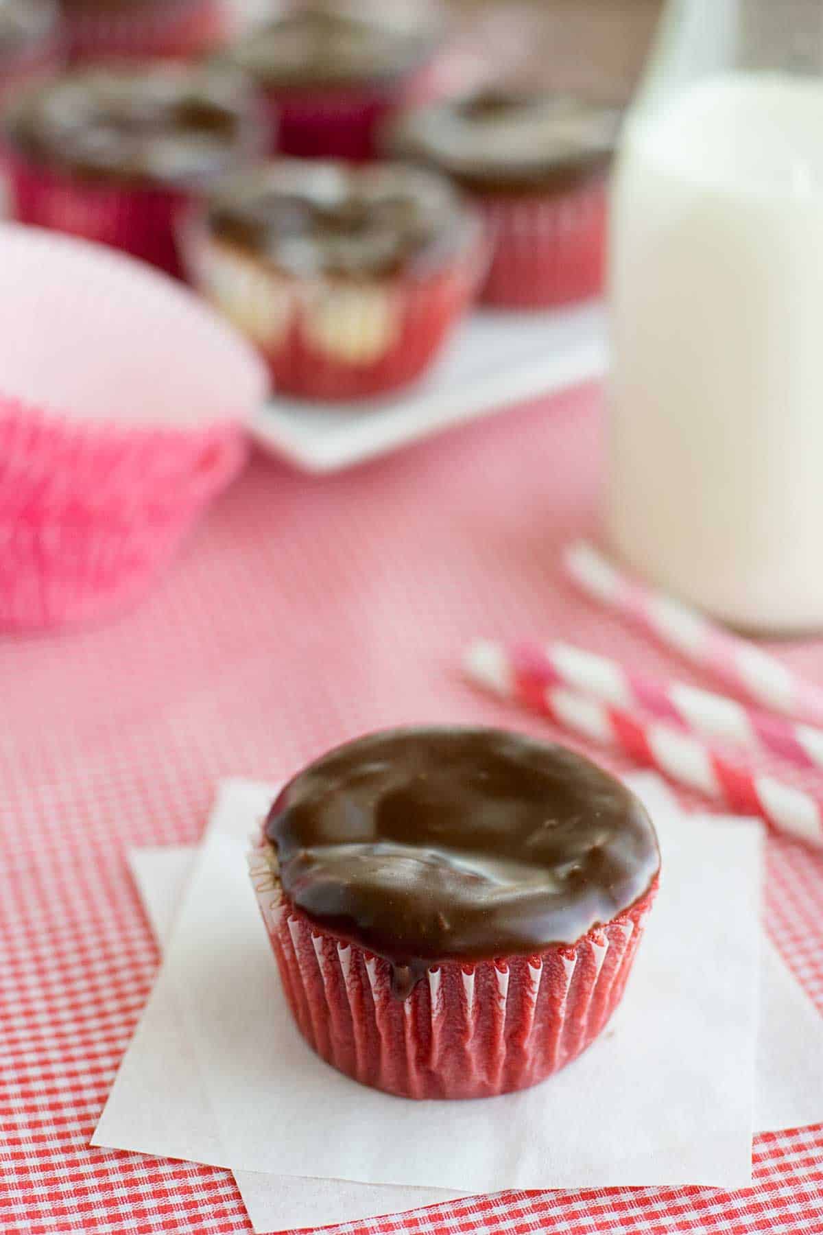 A red velvet cheesecake cupcake topped with chocolate ganache.