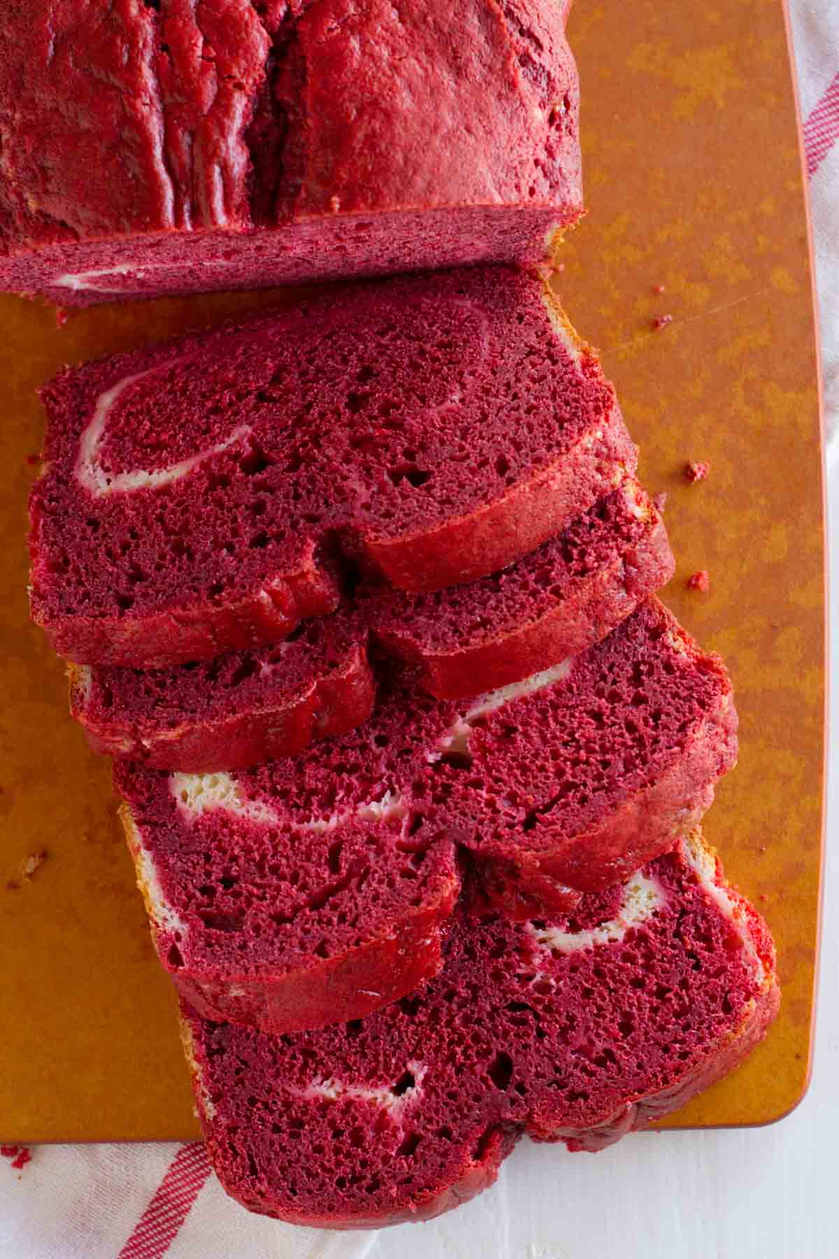 Loaf of red velvet quick bread with cream cheese filling cut into slices.