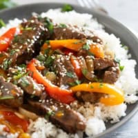 Serving of slow cooker pepper steak over rice, topped with cilantro and sesame seeds.