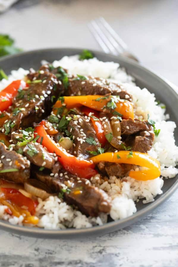 Serving of slow cooker pepper steak over rice, topped with cilantro and sesame seeds.