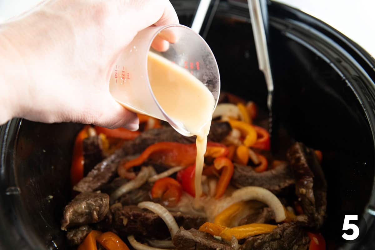 Pouring a cornstarch mixture into a crockpot for Slow Cooker Pepper Steak.