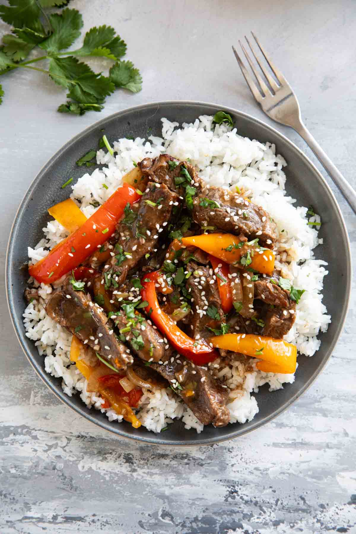 Plate filled with Slow Cooker Pepper Steak over rice, topped with cilantro.