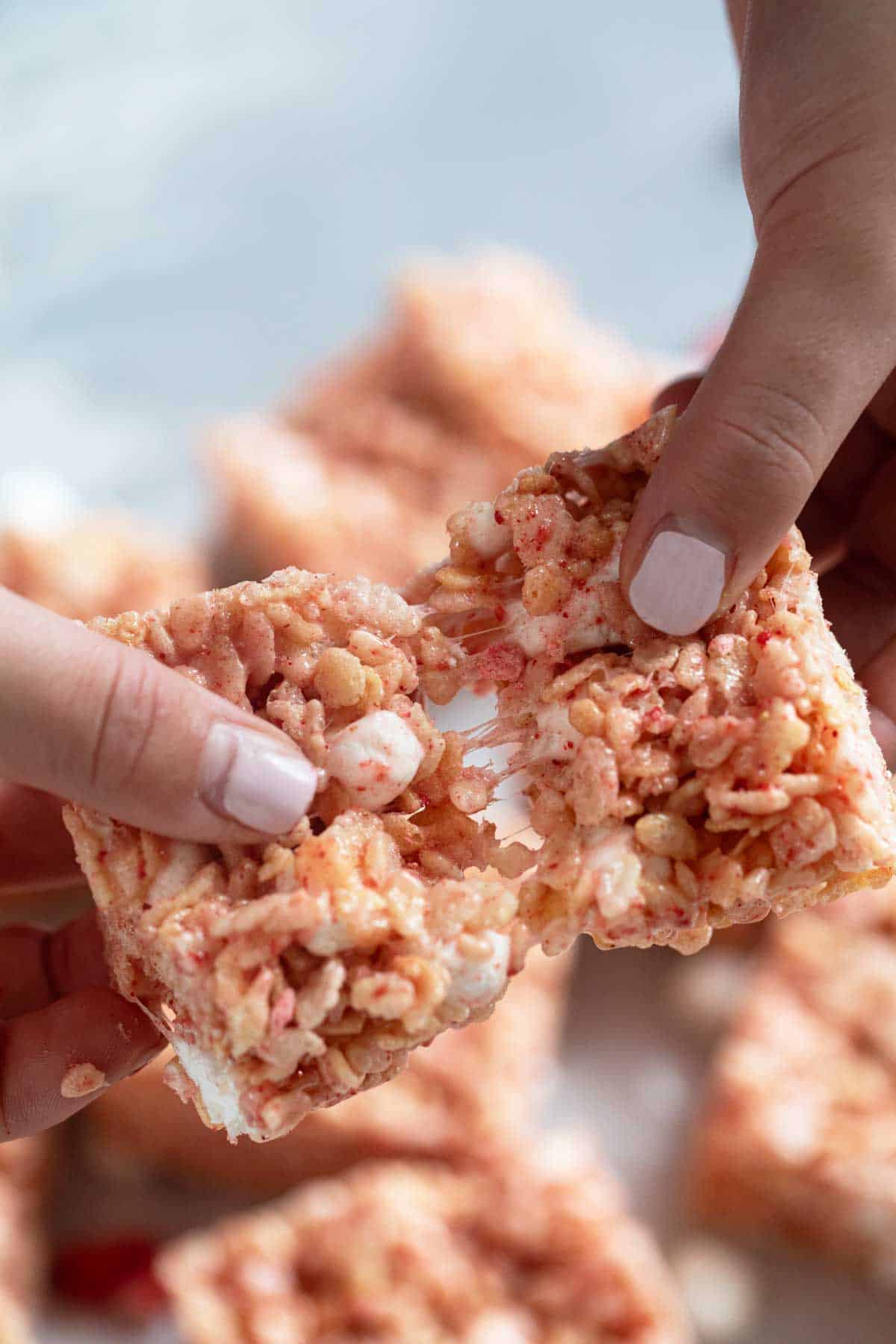 Fingers pulling a strawberry Rice Krispie treat apart.