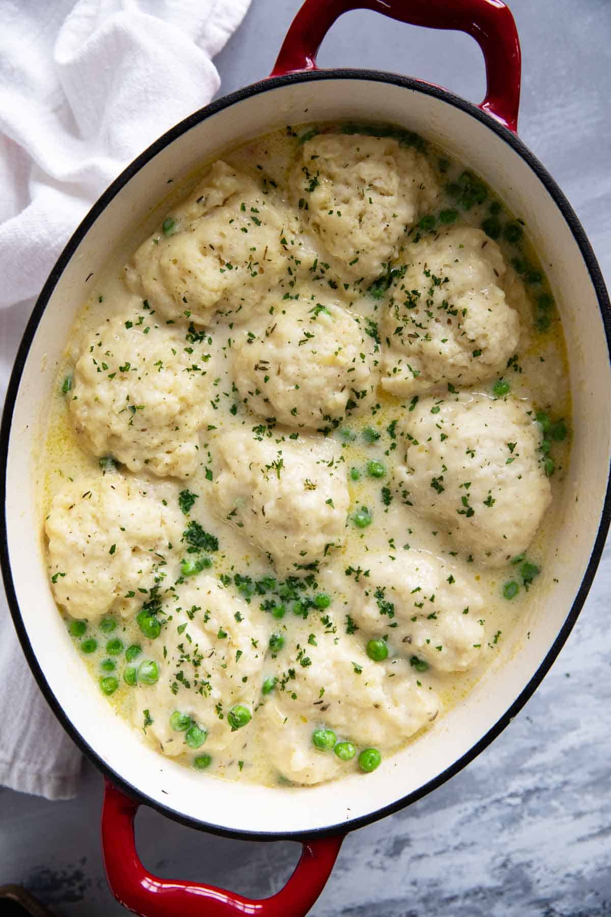 Soup pot filled with chicken and dumplings, topped with fresh herbs.