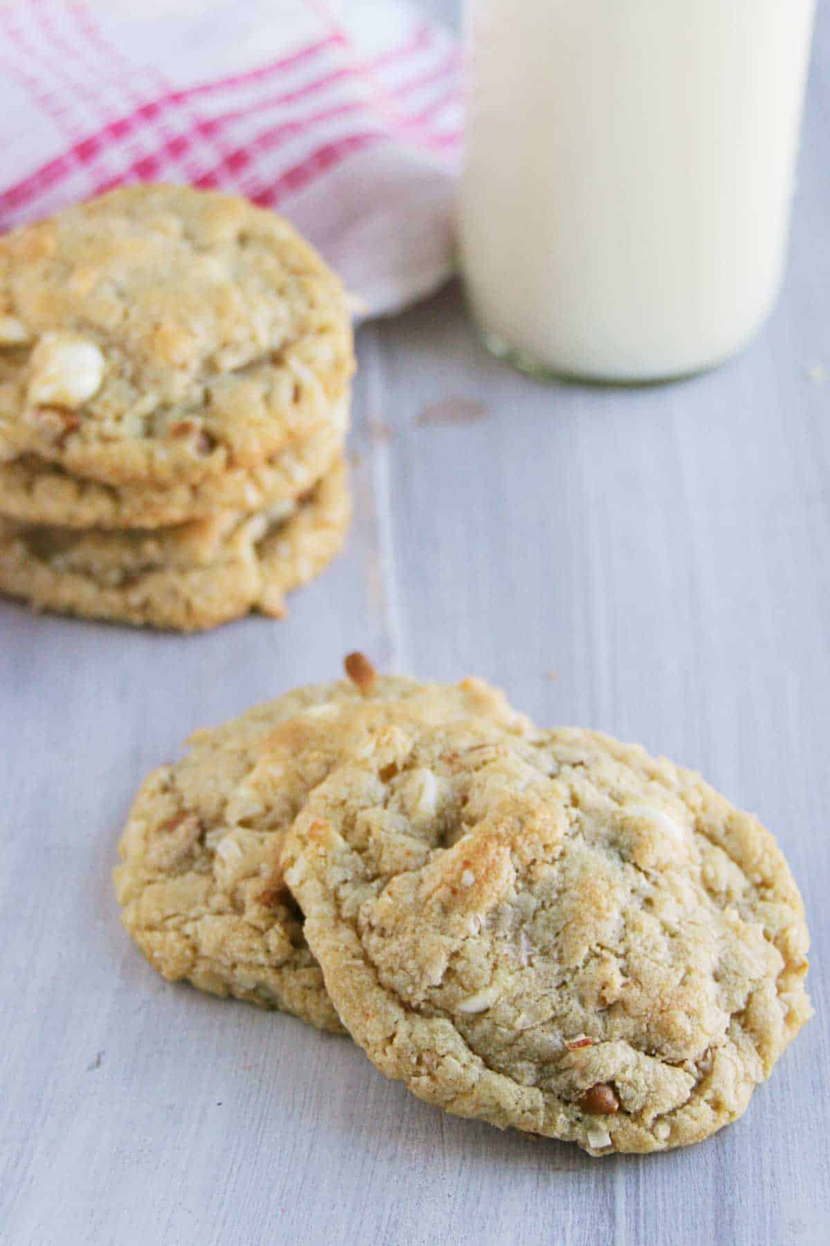 Cinnamon, White Chocolate, and Coconut Oatmeal Cookies on a surface with more stacked behind.