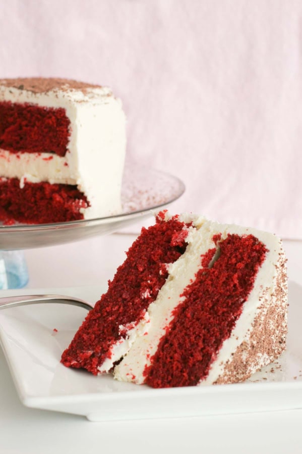 Slice of red velvet cheesecake cake with two layers of cake and one layer of cheesecake.