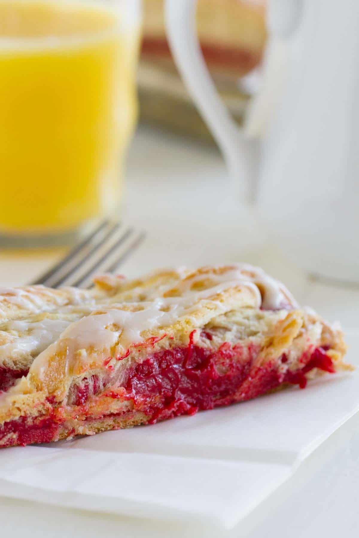 Slice of red velvet cream cheese danish with orange juice in the back.