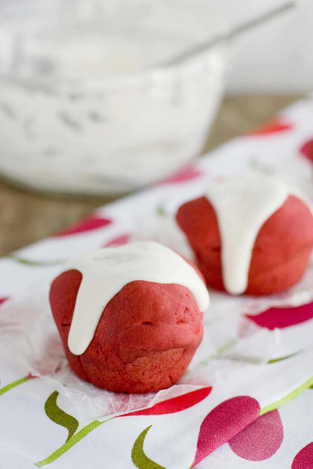 Two red velvet rolls topped with cream cheese glaze.