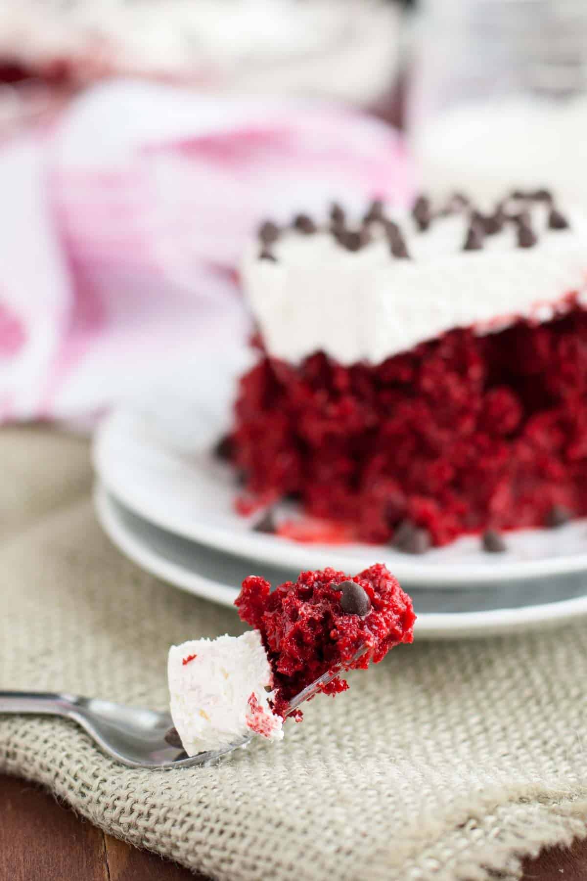 Fork full of a bite of red velvet tres leches cake with whipped topping.