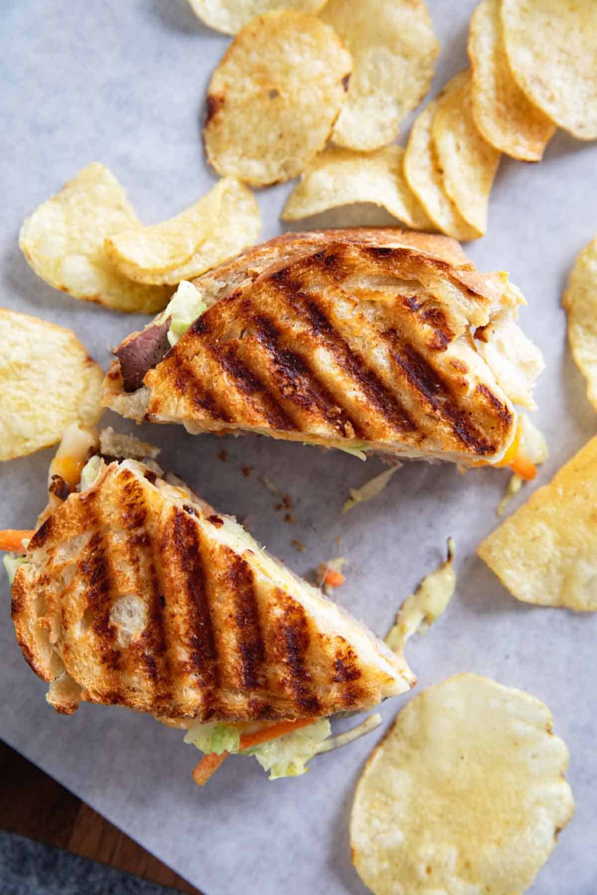 Roast Beef Panini with slaw cut in half, surrounded by potato chips.