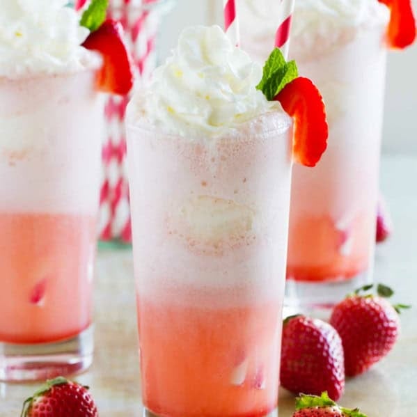 Three strawberry cream floats made with soda, syrup, ice cream, and whipped cream.