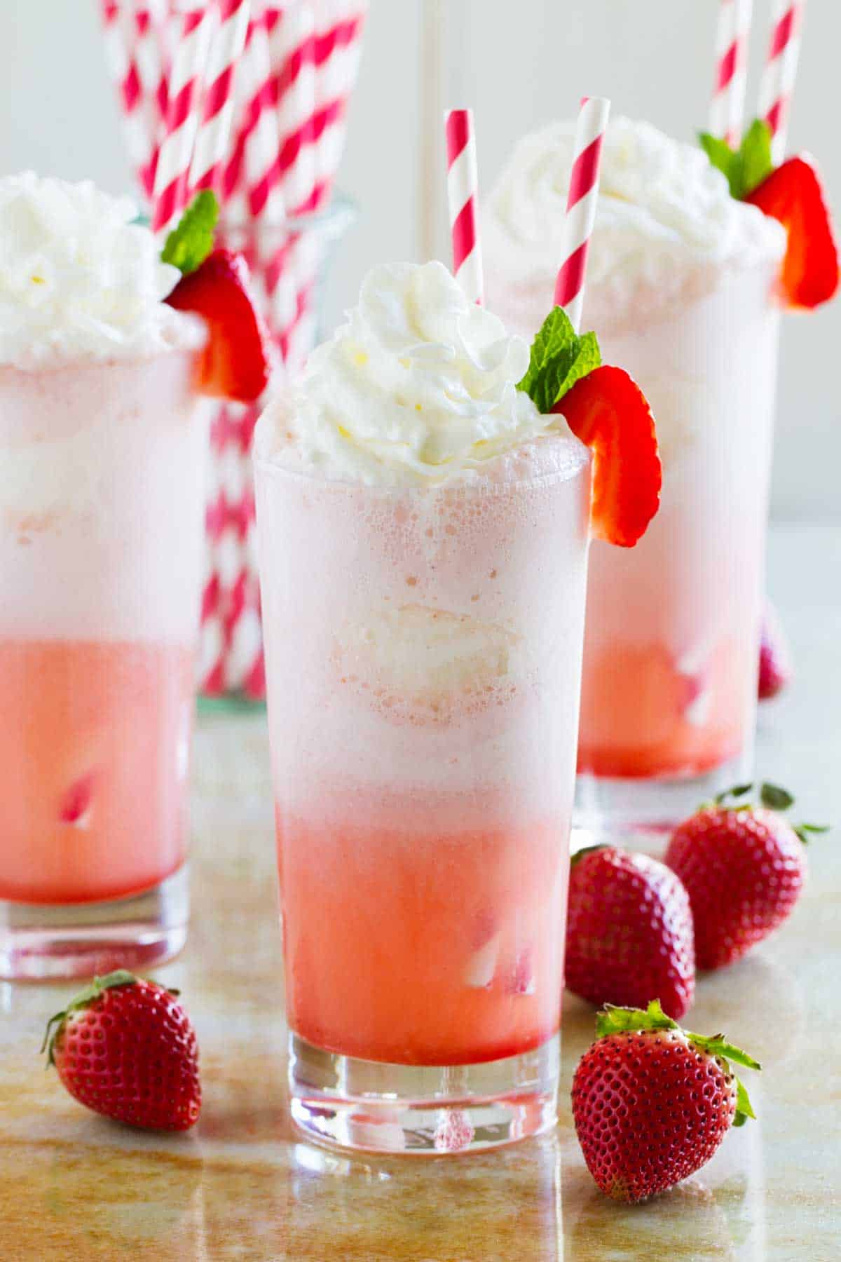 Three strawberry cream floats made with soda, syrup, ice cream, and whipped cream.