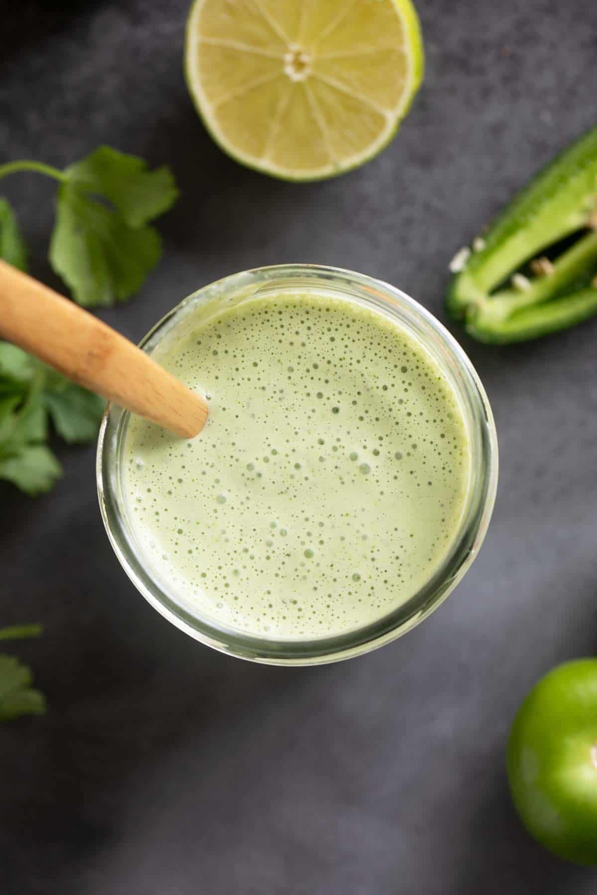 Tomatillo Ranch Dressing in a jar, surrounded by tomatillos, cilantro, limes, and jalapeno.