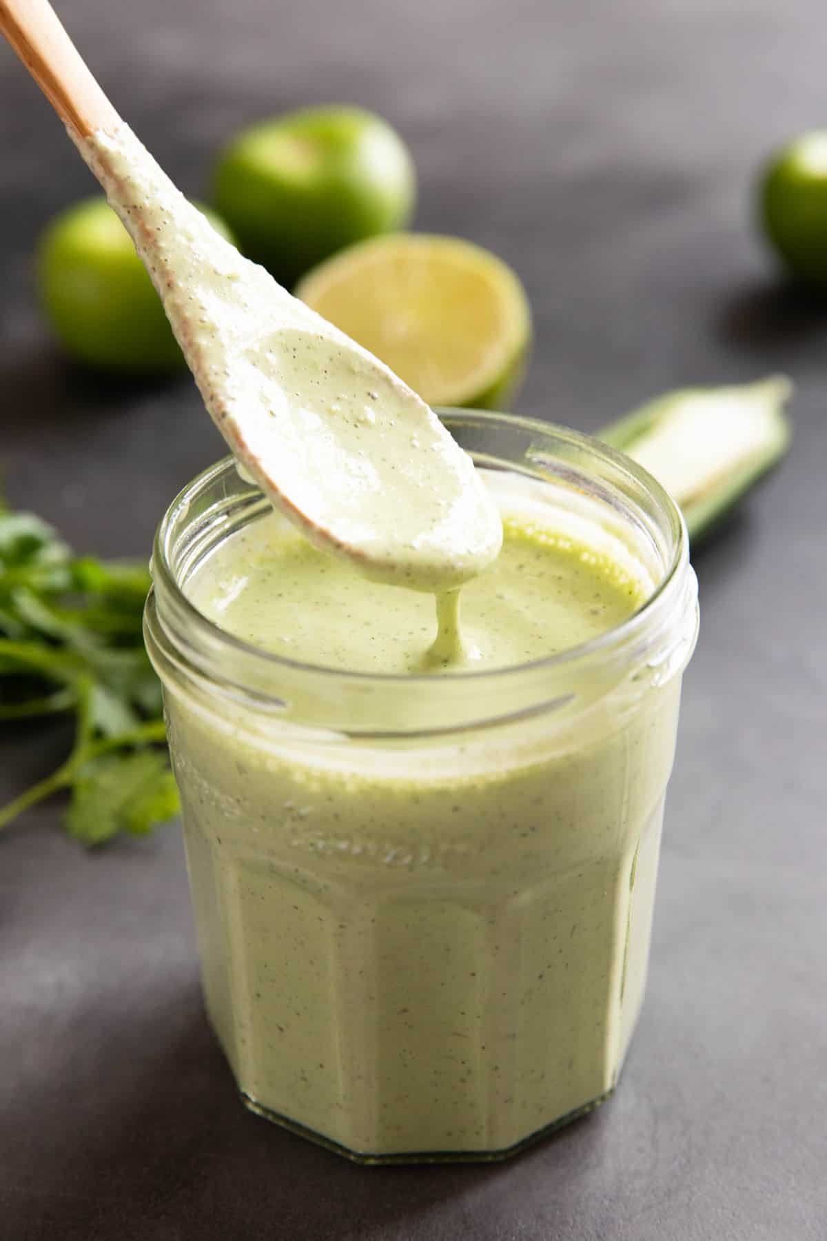 Spoon in tomatillo ranch dressing with some dripping off of the spoon.