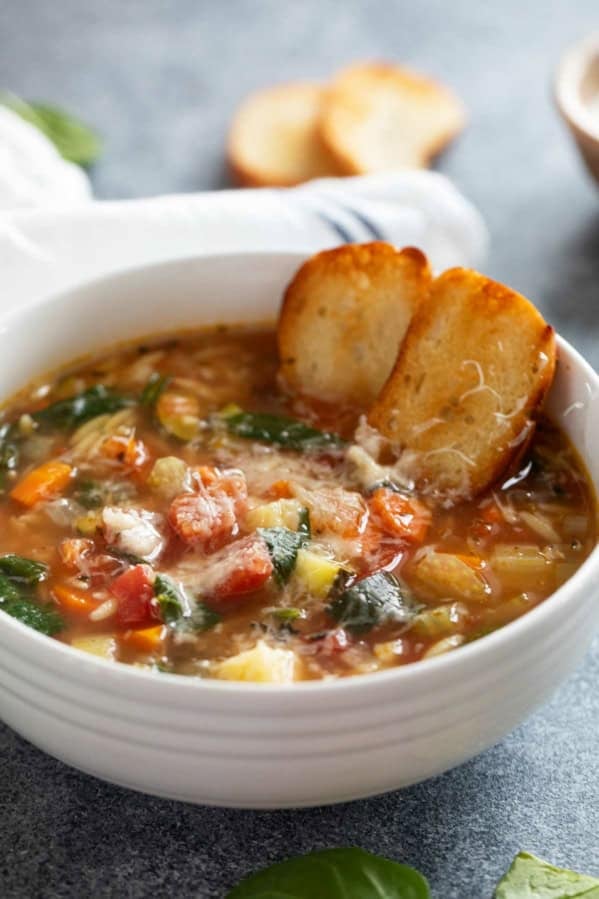 Bowl of Vegetable Soup with Orzo topped with parmesan cheese and toasted bread.