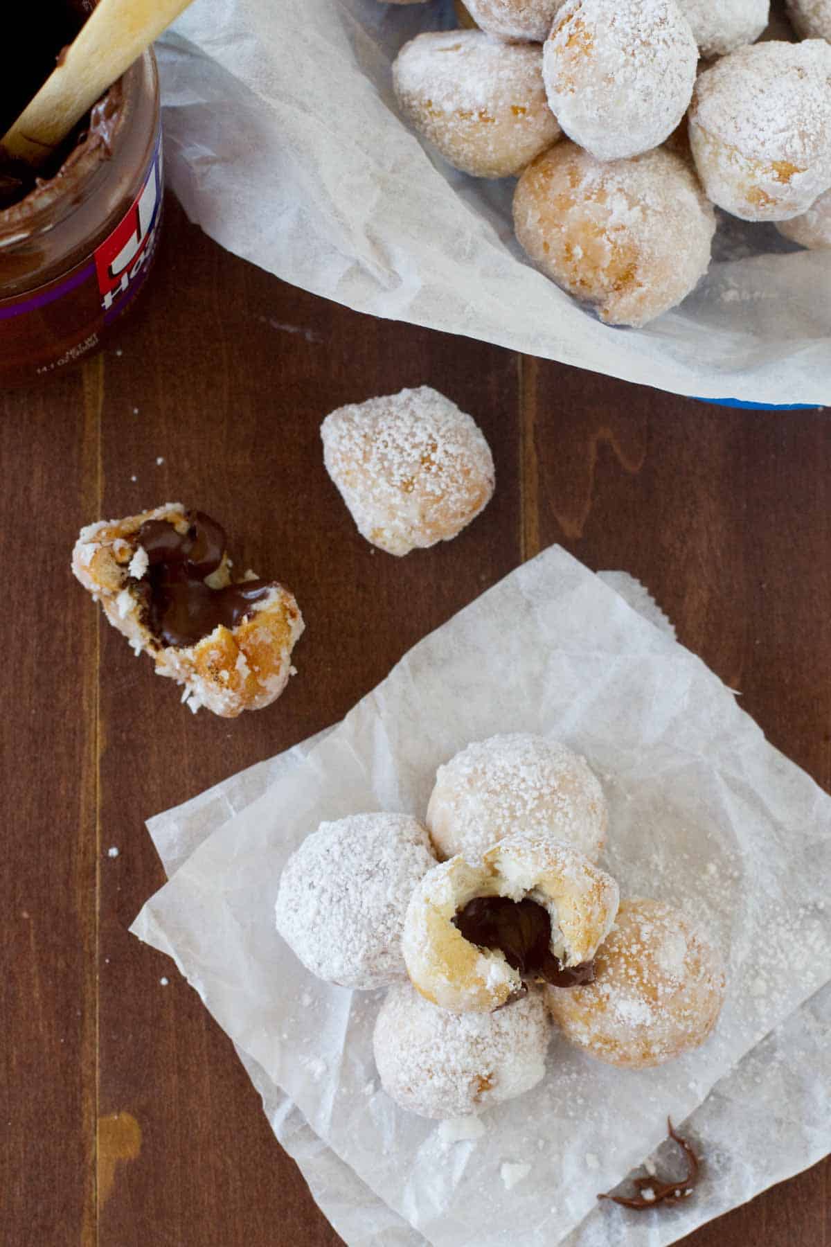 Chocolate Hazelnut Stuffed Donut Holes stacked on parchment paper with one torn open to show chocolate.