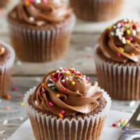 Chocolate Sour Cream Cupcakes with Chocolate Buttercream and rainbow sprinkles on a wooden surface.