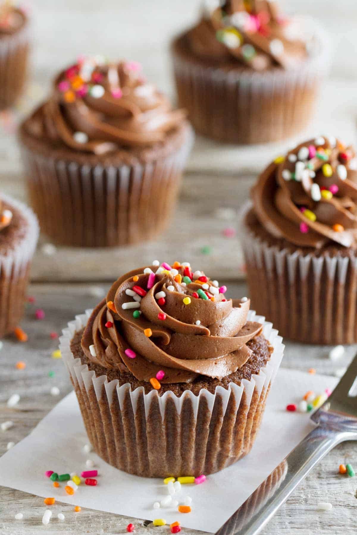 Chocolate Sour Cream Cupcakes with Chocolate Buttercream and rainbow sprinkles on a wooden surface.