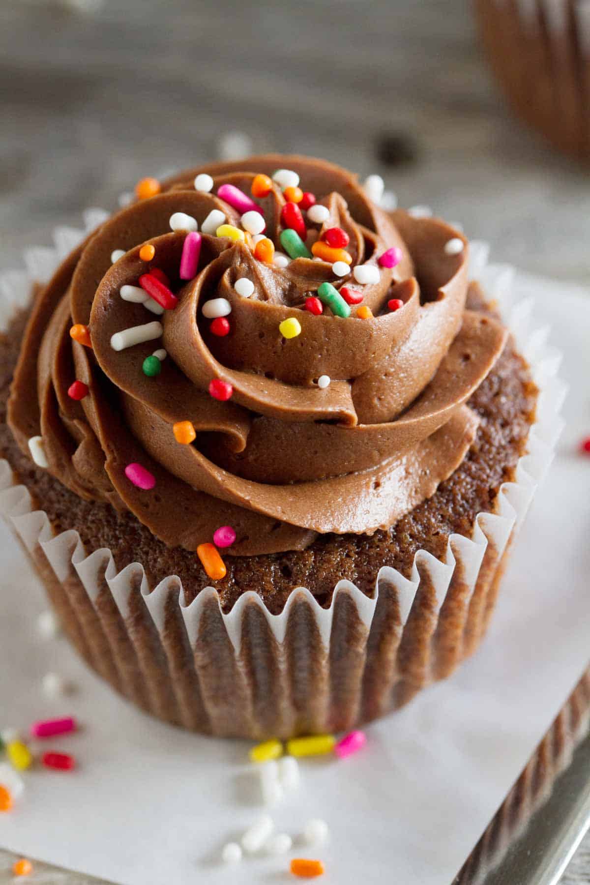 Chocolate Sour Cream Cupcake topped with a smooth chocolate buttercream and rainbow sprinkles.