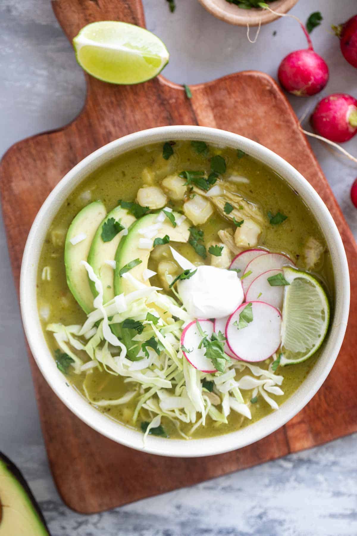 Bowl of Pozole Verde topped with cabbage, radishes, cilantro, and avocado.