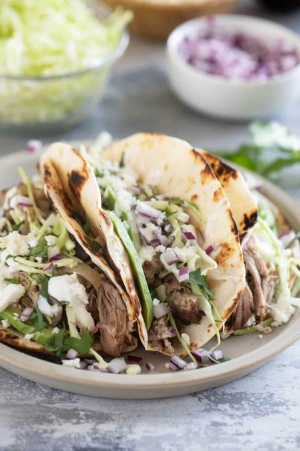 Shredded Pork Tacos topped with cabbage, onions, avocado, and more.