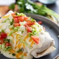 Smothered Burritos with ground beef and refried beans, covered in green Chile sauce, cheese, tomatoes, and lettuce.