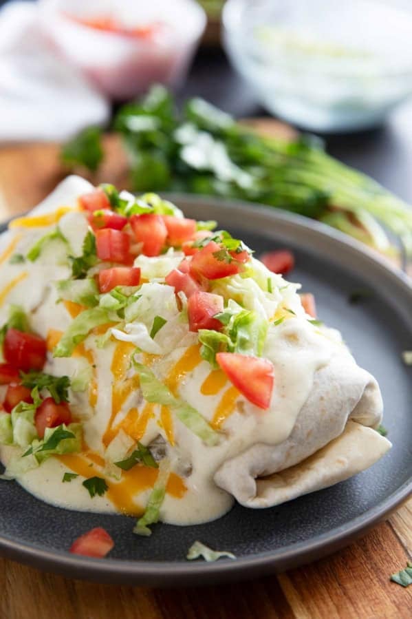 Smothered Burritos with ground beef and refried beans, covered in green Chile sauce, cheese, tomatoes, and lettuce.