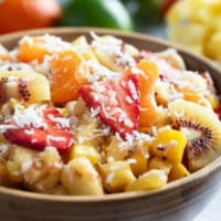 Bowl filled with tropical fruit salad made with strawberries, mango, pineapple, kiwi, oranges, and a sweet dressing.