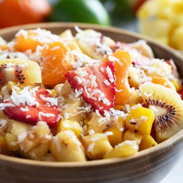 Bowl filled with tropical fruit salad made with strawberries, mango, pineapple, kiwi, oranges, and a sweet dressing.