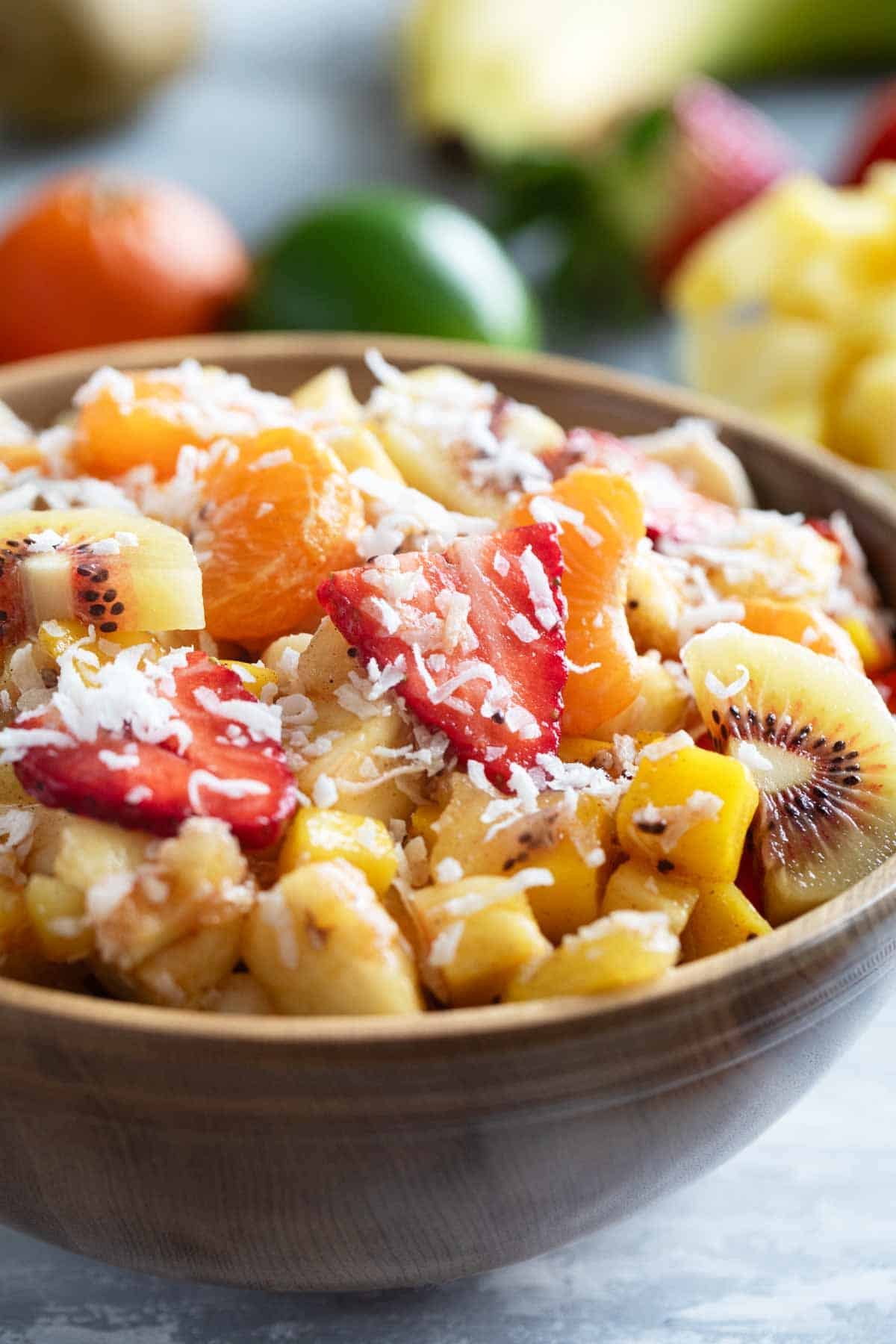 Bowl filled with tropical fruit salad made with strawberries, mango, pineapple, kiwi, oranges, and a sweet dressing.