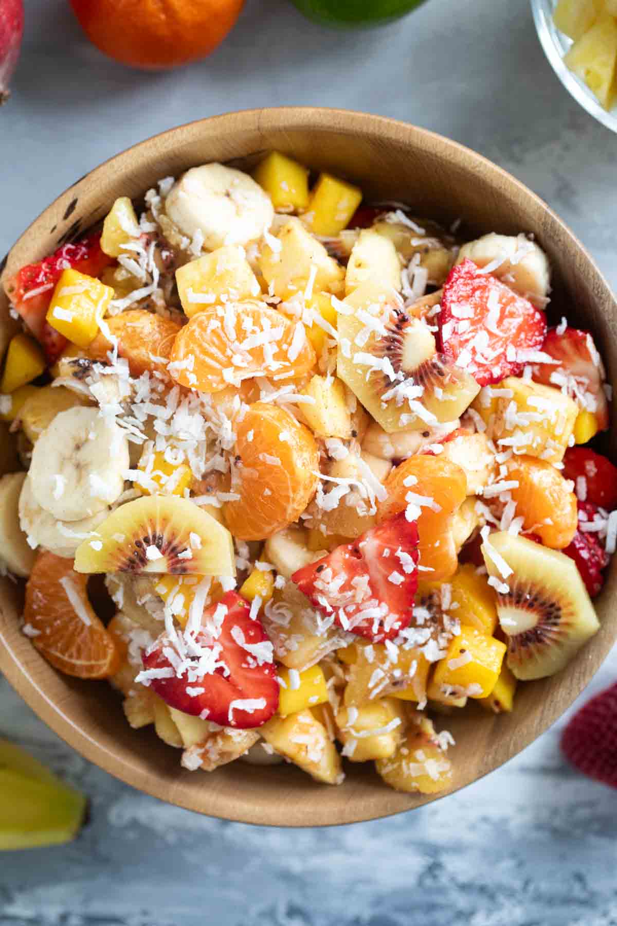 Wooden bowl filled with tropical fruit salad sprinkled with coconut.