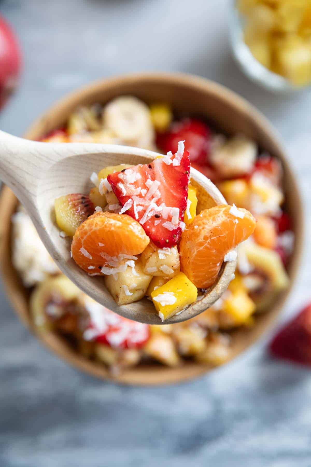 Wooden spoon full of tropical fruit salad with coconut.